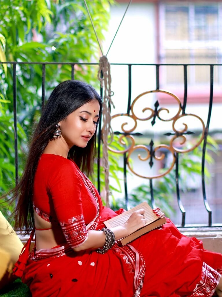 লাল শাড়ি পরে বারান্দায় বসে বই পড়ছেন মোনামি ঘোষ